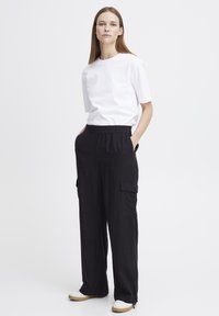 T-shirt blanche à manches courtes avec un col rond, associée à un pantalon cargo noir avec poches latérales, taille élastique et coupe large.