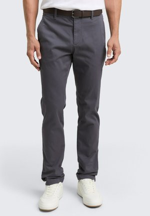 Pantalon gris avec une texture lisse, présentant une coupe classique, des passants de ceinture et des poches avant, associé à des baskets blanches.