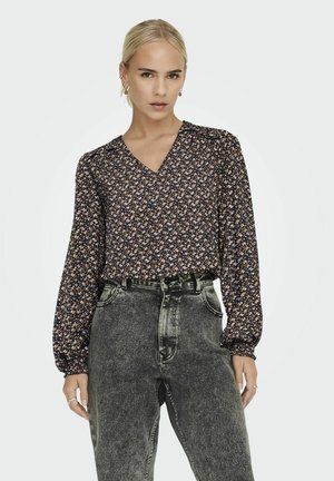 Langsleeve blouse met een v-hals, marineblauwe stof met bloemenpatronen in lichte kleuren. Gecombineerd met high-waisted vervaagde zwarte jeans.