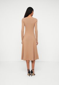 Hosszú ujjú, testhezálló bézs ruha, bővülő szoknyával. Sima kötött anyag és egyszerű, kerek nyakkivágás, fekete magas sarkú szandálokkal párosítva.