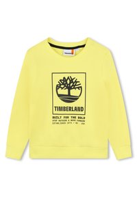 Sweatshirt jaune en tissu doux avec un graphique noir représentant un arbre et le texte : "TIMBERLAND CONÇU POUR LES AUDACIEUX," avec des poignets côtelés.