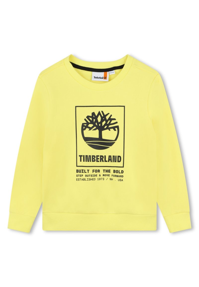 Sweatshirt jaune en tissu doux avec un graphique noir représentant un arbre et le texte : "TIMBERLAND CONÇU POUR LES AUDACIEUX," avec des poignets côtelés.