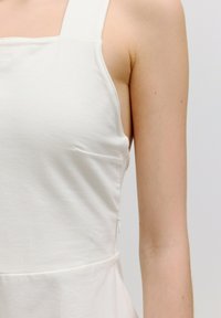 Witte mouwloze top met een rechte halslijn, zijnaaddetails en een zachte textuur, die een getailleerd ontwerp en een klassieke silhouet benadrukt.