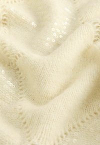 Texturiert, cremefarbener Stoff mit einer weichen, gestrickten Optik, der mit verstreuten weißen Pailletten für zusätzliche Details versehen ist.