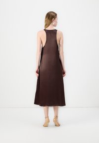 Brun satin slipkjole med scoop rygg, midtlang design og jevn tekstur. Båret med gjennomsiktige heler og minimalistiske smykker.