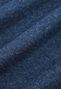 Granatowa dzianina, teksturowana delikatnym prążkowaniem i gładkim wykończeniem. Światło łapie się w włóknach, podkreślając jej miękkość.