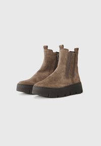 Bottines en suède marron avec semelle compensée. Équipées de zip sur les côtés et de panneaux en élastique pour un enfilage facile. Texture lisse et design à bout rond.