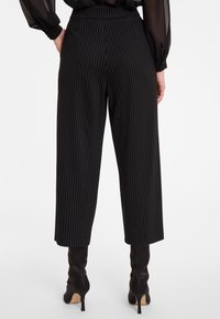 Zwarte broek met streepjes, hoge taille, slim fit en cropped lengte. Draagt met zwarte haklaarzen voor een strakke uitstraling.