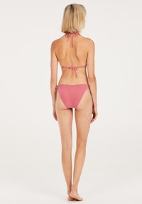 Różowy zestaw bikini z halter topem z wiązaniami i dopasowanymi dolnymi majtkami o niskim stanie. Materiał ma miękką teksturę i minimalny wzór.