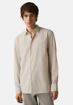Camicia a righe button-up di un beige chiaro con sottili linee verticali. Presenta un colletto classico e polsini con bottone. Tessuto morbido.