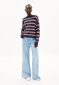 Gestreepte marineblauwe en roze trui met een ontspannen pasvorm, gecombineerd met lichtblauwe denim jeans met wijde pijpen en witte instappers.
