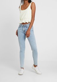 Vaaleankeltainen peplum-toppi teksturoidulla kuviolla, yhdistettynä vaaleansinisiin skinny-farkkuihin ja valkoisiin lenkkareihin.