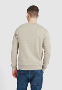 Beżowa bluza z długim rękawem, okrągłym dekoltem i ściągaczami. Noszona z niebieskimi dżinsami, prezentując prosty, casualowy design.