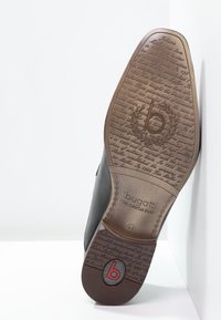 Chaussure noire avec une tige en cuir lisse et une semelle en caoutchouc marron comportant un texte embossé et un accent de logo rond. Taille indiquée 46.