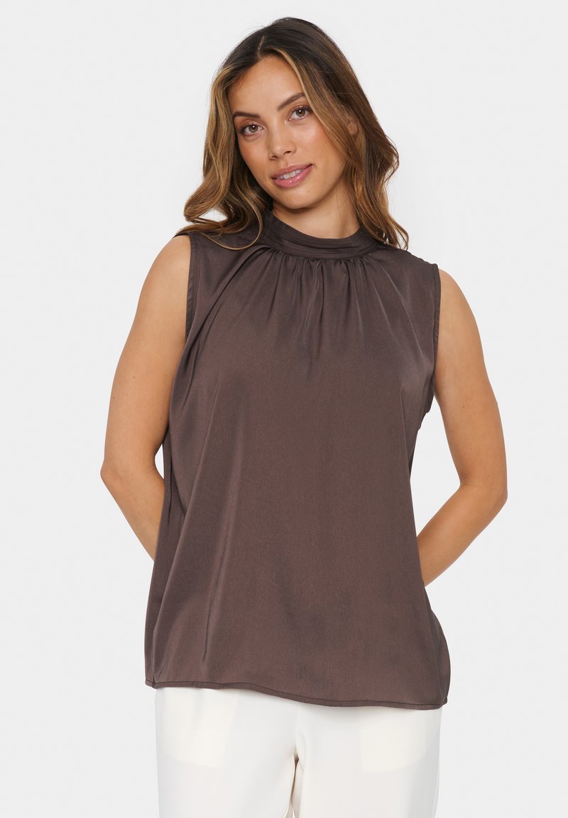 Top senza maniche di colore marrone con collo alto e dettagli arricciati, caratterizzato da una superficie liscia e una vestibilità rilassata, abbinato a pantaloni color crema.
