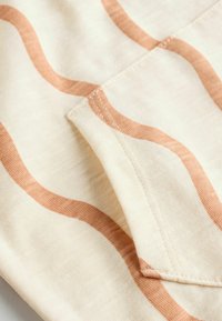 Bomullstyg med vågiga, ljusbruna ränder på en krämfärgad bakgrund, med synliga sömmar och mjuk textur.
