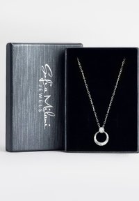 Sølv halskæde med en cirkulær vedhæng, der har et tekstureret design og en central krystal, præsenteret i en sort fløjlskasse.