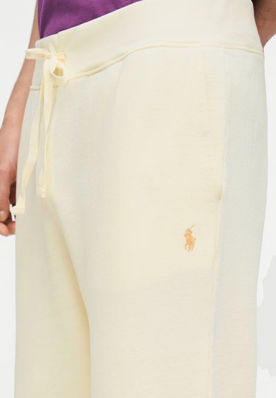 Κοντινό πλάνο ανοιχτόκίτρινων φόρμας με κορδόνι στη μέση και κεντημένο λογότυπο παίκτη πόλο κοντά στην εμπρόσθια τσέπη.