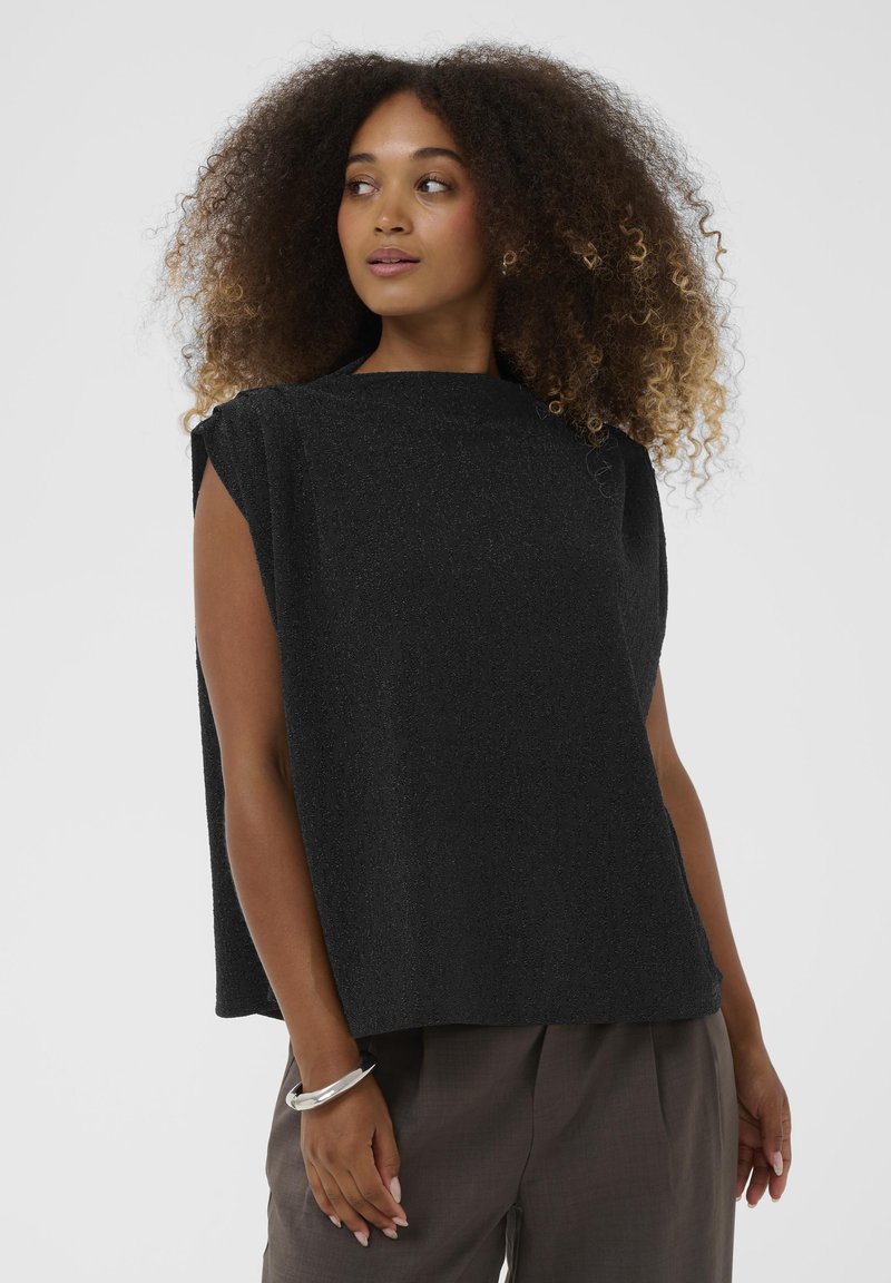 Mustamat ilma varrukatop, millel on kõrge kaelus, tekstureeritud kangas ja õlavarre aktsentdetailid. Kombineeritud lõdva tumeda püksiga.