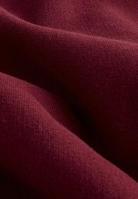 Tessuto a maglia borgogna con una superficie morbida e testurizzata, che mostra un motivo liscio e leggermente in rilievo in diverse luci.