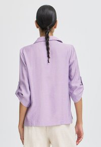 Blusa a maniche lunghe viola chiaro con vestibilità ampia, dotata di colletto, maniche arrotolabili e texture liscia, realizzata in tessuto leggero.