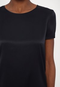 Mørkeblå kortermet topp laget av glatt stoff. Har rund hals og løs passform. Minimalistisk design uten ekstra mønster eller aksenter.