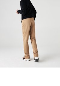 Béžové kalhoty s hladkým povrchem, slim fit a se zadními kapsami. V kombinaci s černobílými botami se vzorem.