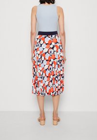 Top in azzurro chiaro abbinato a una gonna plissettata con un motivo floreale nelle tonalità di rosso, blu navy e azzurro chiaro. Sandali con tacco largo.