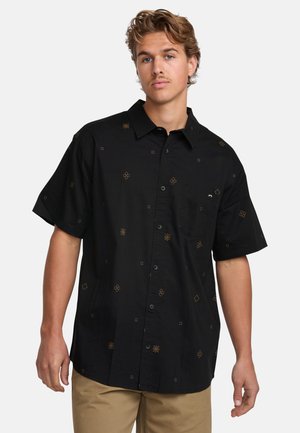 Camisa negra de manga corta hecha de tela ligera, con patrones geométricos dorados, botones en el frente y un bolsillo en el pecho.