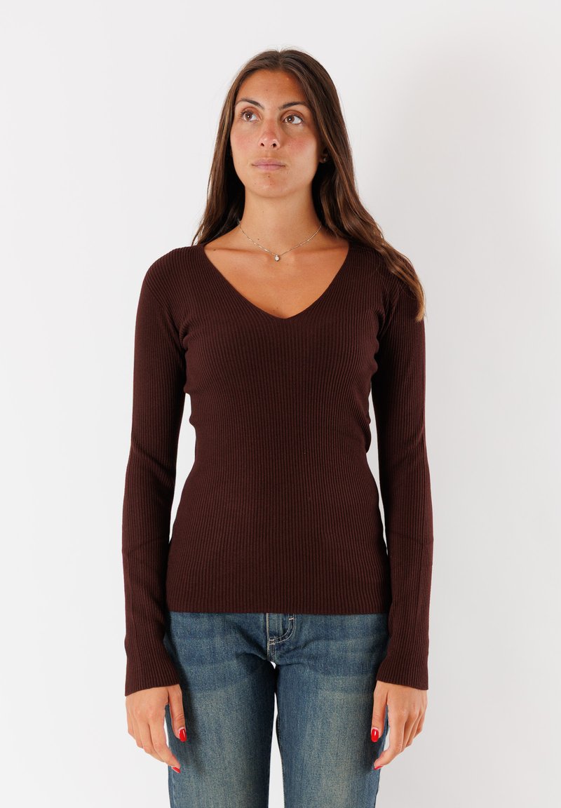 Maglietta lunga a maniche con costine color marrone, scollo a V profondo, silhouette aderente e texture morbida, abbinata a jeans blu.