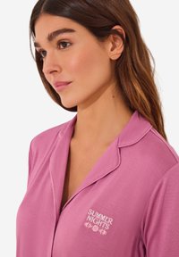 Roze pyjamablouse met een kraag en geborduurde "ZOMERAVONDEN" opdruk. Glad materiaal met een relaxte pasvorm en subtiele glans.