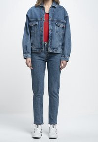 Chaqueta de mezclilla con un corte relajado, que cuenta con dos bolsillos en el pecho, cierres de botones y un lavado azul vintage. Combinada con jeans azules a juego y zapatillas blancas.