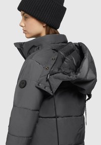 Gray padded jacket with a high collar, adjustable hood, and black buttons. Features a textured black knit beanie.