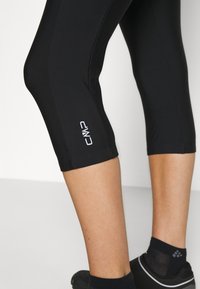Leggings cortos negros hechos de tejido elástico, con una textura suave y un logo blanco en el dobladillo inferior. Diseño ajustado.