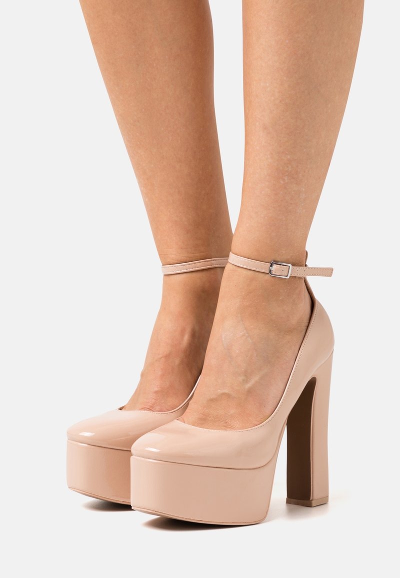 Chaussures à talons hauts en cuir verni couleur chair, avec une semelle plateforme épaisse et une bride de cheville réglable. Design à bout arrondi et texture lisse.