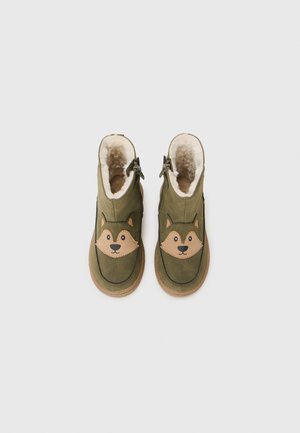Bottes de cheville vertes avec une surface texturée, présentant un design de visage de renard tan et une doublure en fausse fourrure. Zips sur les côtés et semelles en caoutchouc pour une meilleure adhérence.