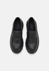Paire de mocassins noirs en cuir à enfiler avec bouts arrondis et semelles en caoutchouc texturées, vus de dessus sur un fond neutre.
