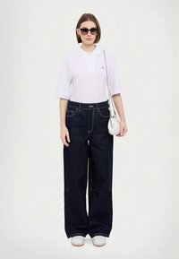 Valge polosärk, tumesinised laia säärega teksapüksid, valged tennised ja päikeseprillid. Särgil väike logo. Lihtne risti kantav kott.