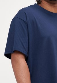 Tmavě modré bavlněné tričko s volnějším střihem, krátkými rukávy a kulatým výstřihem. Hladká textura s viditelnými švy.