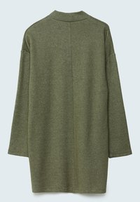 Pitkähiha, oliivinvihreä neuleliivi, jossa on suora sauma selkäpuolella, esitettynä litteänä vaaleaa taustaa vasten.