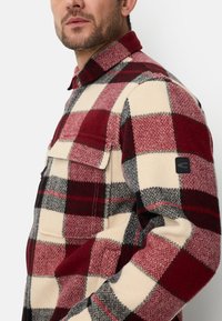 Rød, creme og grå ternet flannel-skjorte med knaplukning på kraven, forlommer og et mærkepatch på ærmet. Tekstureret stof.