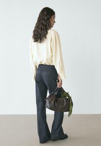 Hellgelbes übergroßes Hemd, dunkelblaue hoch taillierte Schlagjeans, braune strukturierte Handtasche mit grünem Bandana-Akzent, von hinten gesehen.