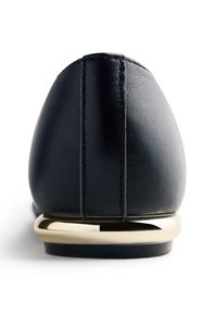 Chaussure plate en cuir noir avec un embout arrondi, couture visible et un accent doré métallique sur le talon. Texture lisse et design classique.
