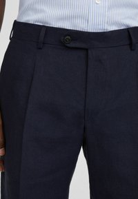 Pantaloni in lino blu navy con una texture liscia, dotati di pieghe frontali, chiusura con bottone e tasche laterali.