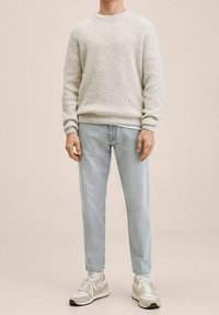 Maglione lavorato a maglia grigio chiaro, jeans azzurri a gamba stretta e sneakers bianche con dettagli beige. Design semplice e casual.