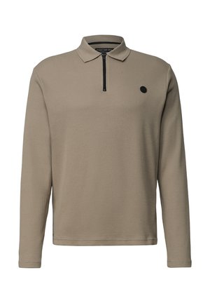 Mand iført beige langærmet strikket polo med sort kvart-lynlås og lille sort cirkulært logo på brystet.