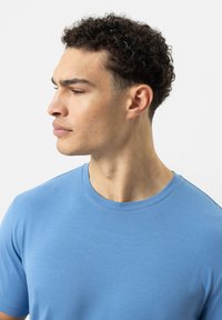 Helles blaues T-Shirt mit Rundhalsausschnitt aus weichem Stoff, mit kurzen Ärmeln und glatter Textur, an einem Modell im Profil gezeigt.