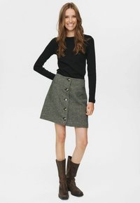 Fustă gri cu model houndstooth, cu formă în A, închidere frontală cu nasturi și două buzunare laterale, asortată cu un top negru cu mânecă lungă și cizme maro.