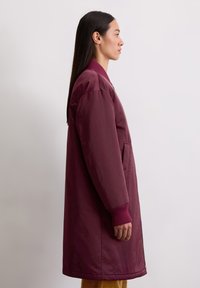 Bordeaux, langharige bovenkleding met een ontspannen pasvorm, ribgebreide manchetten en zijzakken; soepele textuur met een ritsluiting.