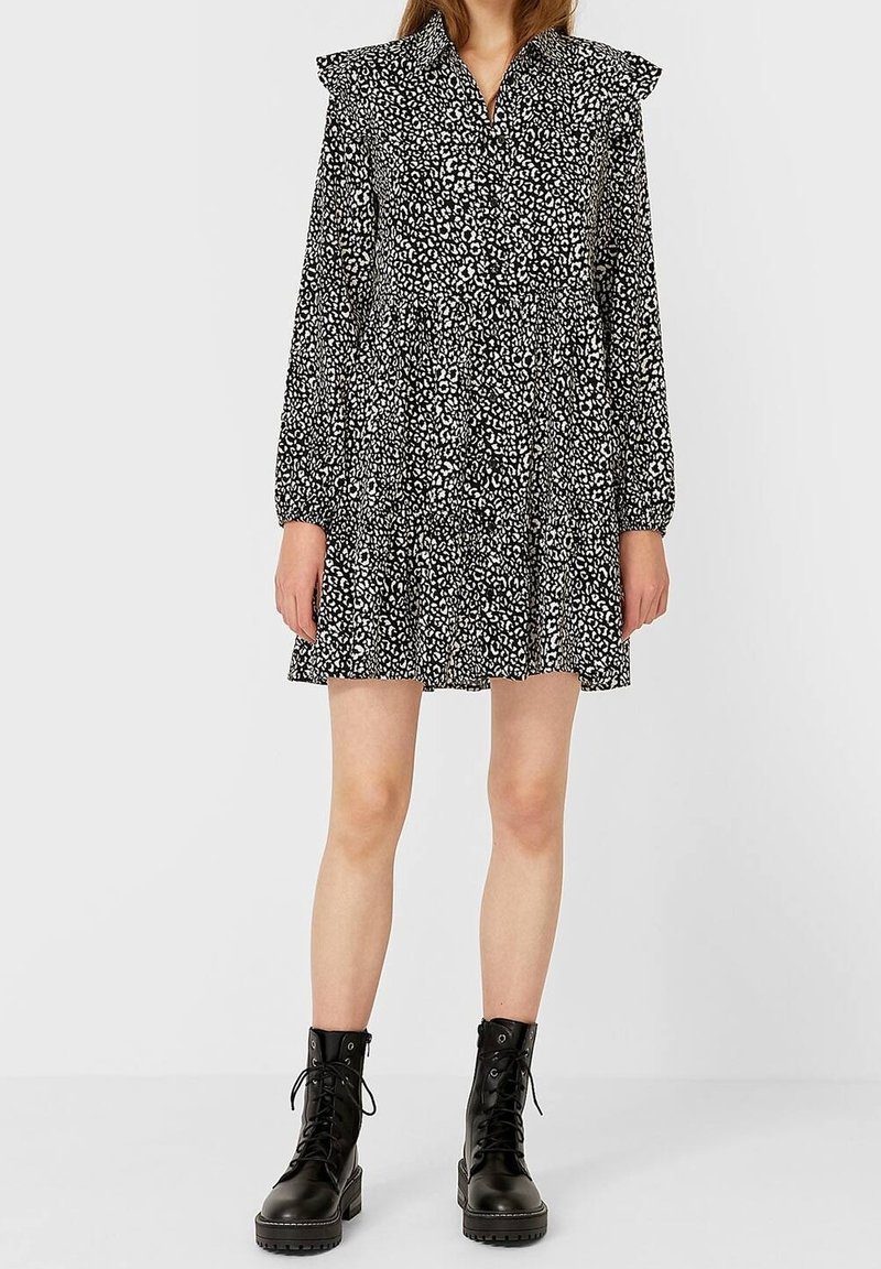 Femme portant une robe imprimée léopard noir et blanc avec des manches longues et des épaulettes volantées, associée à des bottines noires à lacets.